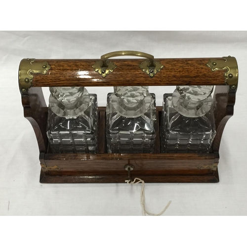 23 - A VINTAGE MAHOGANY TANTALUS DECANTER SET WITH BRASS DETAILING AND A KEY