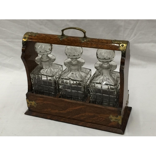 23 - A VINTAGE MAHOGANY TANTALUS DECANTER SET WITH BRASS DETAILING AND A KEY