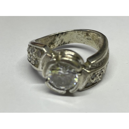 586 - A SILVER RING WITH A LARGE CENTRAL CLEAR STONE AND CLEAR SONES ON TWISTED SHOULDERS SIZE O/P IN A PR... 