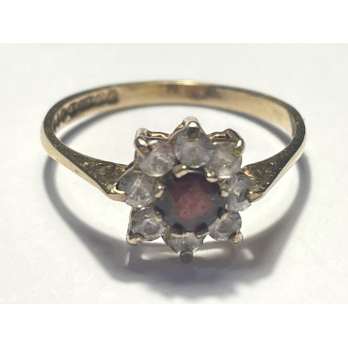 571 - A 9 CARAT GOLD RING WITH A CENTRE RED STONE SURROUNDED BY EIGHT CLEAR STONES IN A FLOWER DESIGN SIZE... 