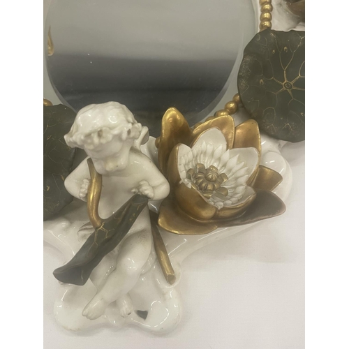 24 - A WHITE AND GILDED CERAMIC MIRROR WITH CHERUB, LILY AND LEAF DESIGN (A/F CHERUBS ARM)