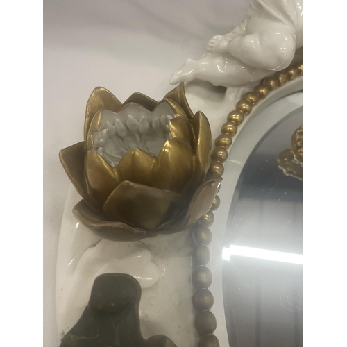 24 - A WHITE AND GILDED CERAMIC MIRROR WITH CHERUB, LILY AND LEAF DESIGN (A/F CHERUBS ARM)