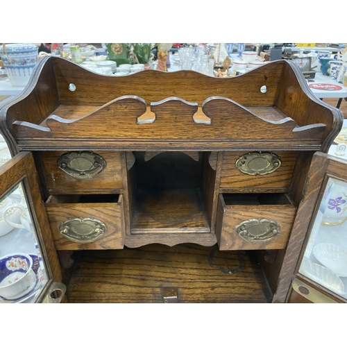 95 - A VINTAGE OAK SMOKERS CABINET WITH BEVELLED GLASS DOORS, BRASS HANDLED DRAWERS, GALLERIED TOP, ETC H... 