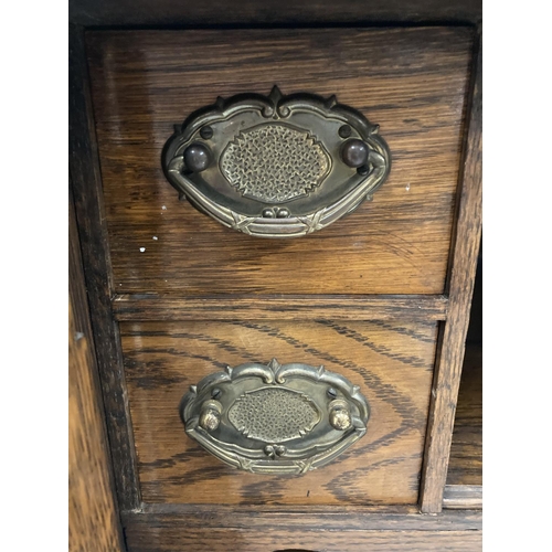 95 - A VINTAGE OAK SMOKERS CABINET WITH BEVELLED GLASS DOORS, BRASS HANDLED DRAWERS, GALLERIED TOP, ETC H... 