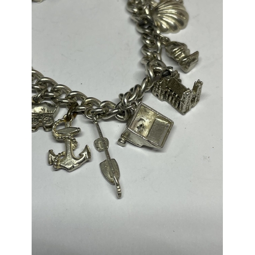 572 - A MARKED SILVER CHARM BRACELET WITH THIRTEEN CHARMS AND A HEART SHAPED CLASP