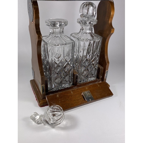 12 - A WOODEN AND SILVER PLATED TWIN BOTTLE TANTLUS WITH TWO CUT GLASS DECANTERS, (ONE STOPPER A/F), MAKE... 