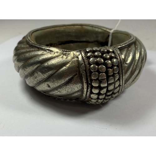 648 - A VINTAGE TRIBAL ORNATE BANGLE, TESTED SILVER