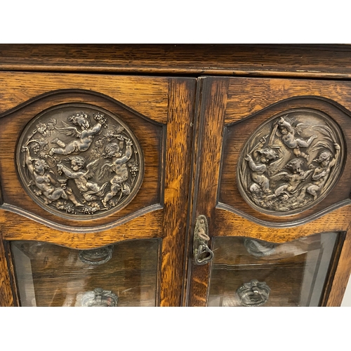 69 - A VINTAGE OAK SMOKERS CABINET WITH CHERUB DESIGN CIRCULAR PLAQUES, INNER DRAWERS AND PULL OUT TRAY, ... 