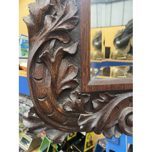 82 - A CARVED OAK MIRROR WITH FOLIATE DECORATION