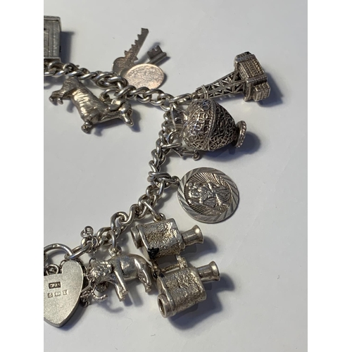 613 - A SILVER CHARM BRACELET WITH FIFTEEN CHARMS AND A HALLMARKED BIRMINGHAM SILVER HEART LOCK