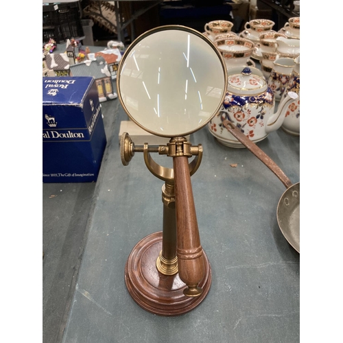 296 - A BRASS MAGNIFYING GLASS ON A GLASS STAND AND WOODEN BASE