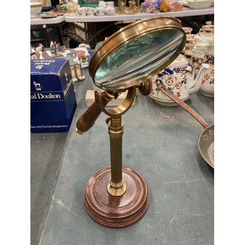 296 - A BRASS MAGNIFYING GLASS ON A GLASS STAND AND WOODEN BASE