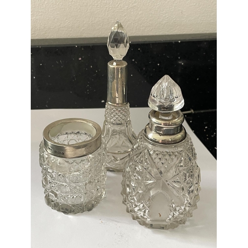 86 - THREE CUT GLASS ITEMS TO INCLUDE A JAR WITH A HALLMARKED BIRMINGHAM COLLAR, A BOTTTLE WITH A HALLMAR... 