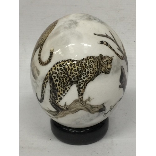 12 - A HAND PAINTED OSTRICH EGG ON STAND WITH CHEETAH DESIGN, INDISTINCTLY SIGNED