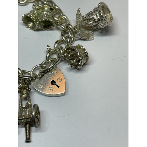 604 - A SILVER CHARM BRACELET WITH ELEVEN CHARMS AND A HEART PADLOCK