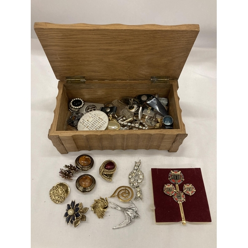 137 - A WOODEN BOX CONTAINING A QUANTITY OF COSTUME JEWELLERY TO INCLUDE BROOCHES, BADGES, CUFFLINKS, EARR... 