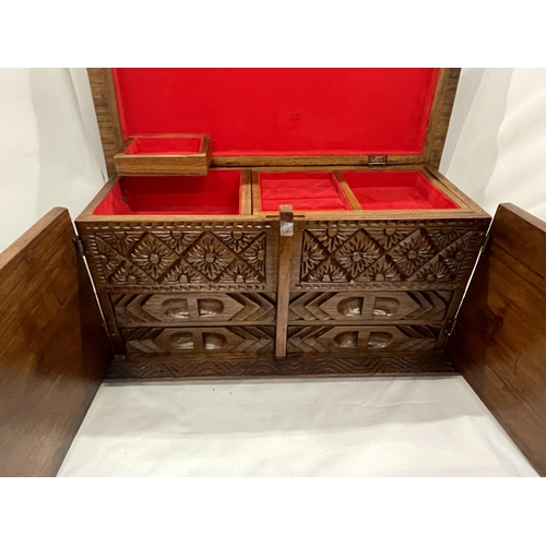 30 - A HEAVILY CARVED JEWELLERY BOX WITH TWO DOORS REVEALING FOUR LINED DRAWERS AND A LIFT UP LID WITH LI... 