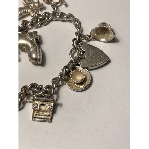 711 - A SILVER CHARM BRACELET WITH ELEVEN CHARMS AND A HALLMARKED BIRMINGHAM SILVER HEART PADLOCK