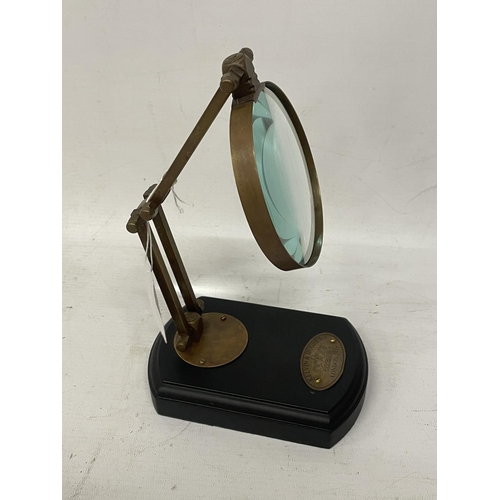 142 - A BRASS MAGNIFYING GLASS ON A WOODEN BASE