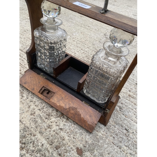 1595 - A VINTAGE OAK TANTALUS DECANTER HOLDER WITH TWO GLASS DECANTERS AND SILVER PLATE DETAIL