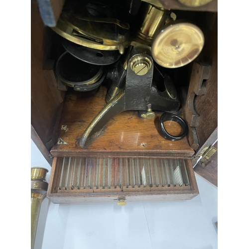 7 - A VINTAGE BRASS MICROSCOPE IN AN OAK BOX WITH A DRAWER OF SLIDES AND TWO FURTHER FITMENTS