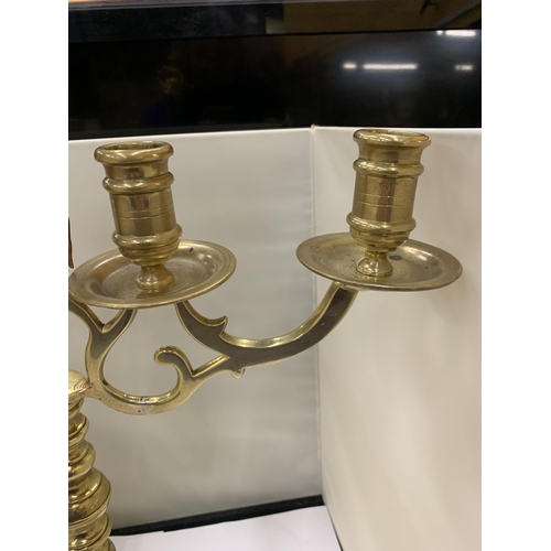 12 - A HEAVY BRASS CANDELABRA WITH A FIGURE HOLDING A STAFF