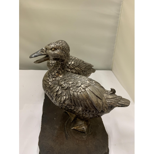 23 - A VINTAGE PAIR OF WHITE METAL DUCKS ON A WOODEN PLINTH