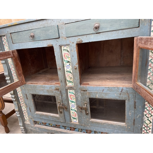 2936 - A VINTAGE INDIAN HARDWOOD CABINET ENCLOSING FOUR GLAZED CUPBOARDS AND TWO DRAWERS WITH INSET COLOURE... 