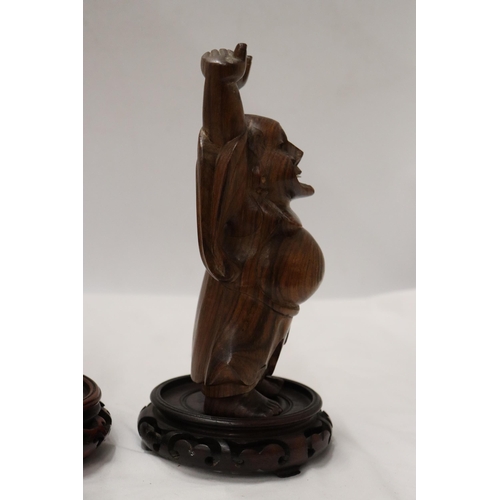 176 - TWO CARVED WOODEN ORIENTAL FIGURES TO INCLUDE A LAUGHING BUDDAH, ON STANDS