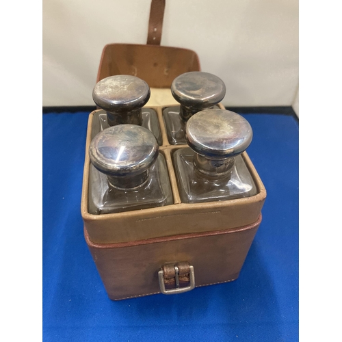 1 - A VINTAGE LEATHER CASE CONTAINING FOUR GLASS BOTTLES WITH HALLMARKED SILVER TOPS