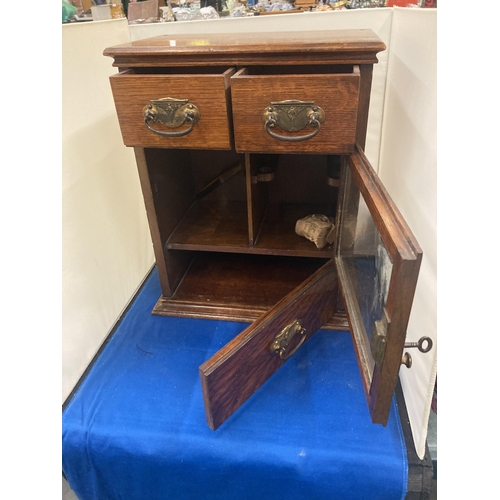 42 - A VINTAGE OAK SMOKERS CABINET WITH TWO SHORT UPPER DRAWERS, A GLAZED DOOR AND A LONG LOWER DRAWER AN... 