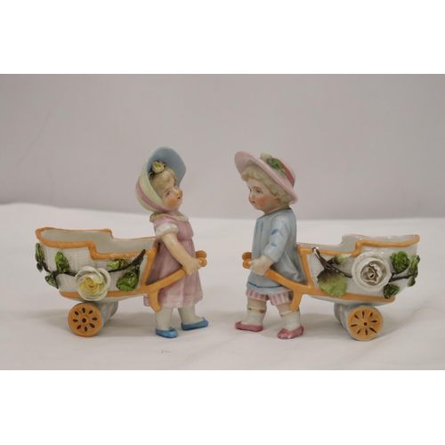 963 - TWO VINTAGE CONTA AND BOHME GERMAN FAIRINGS TO INCLUDE TWO GIRLS PULLING FLOWER CARTS, ONE WITH A HA... 