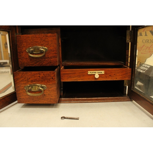 52 - AN OAK TWO GLASS DOOR SMOKERS CABINET WITH THREE INTERIOR DRAWERS ONE LABELED PLAYING CARDS COMPLETE... 