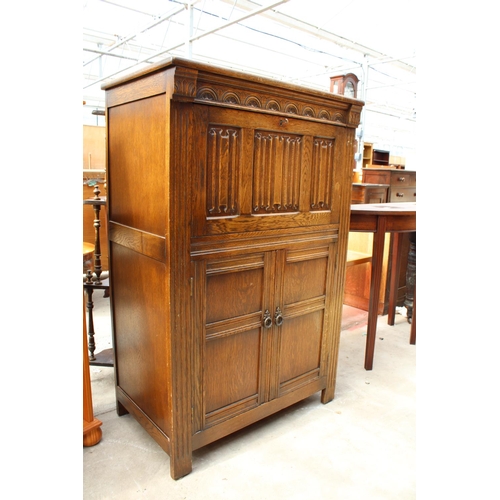 2555 - AN OAK CHARM STYLE COCKTAIL CABINET WITH LINEN-FOLD DROP DOWN FRONT AND CUPBOARD TO BASE, 31.5