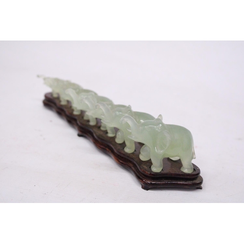 385 - SEVEN GRADUATING JADE ELEPHANTS ON A WOODEN PLINTH (1 A/F)