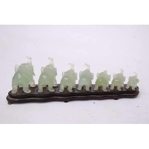 385 - SEVEN GRADUATING JADE ELEPHANTS ON A WOODEN PLINTH (1 A/F)