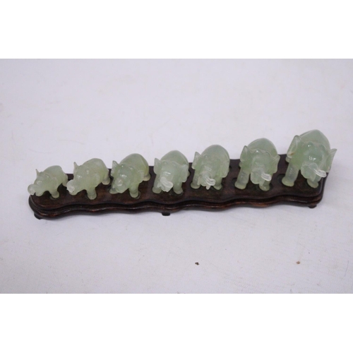 385 - SEVEN GRADUATING JADE ELEPHANTS ON A WOODEN PLINTH (1 A/F)