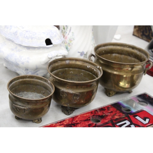 216 - THREE GRADUATED BRASS FOOTED AND HANDLED POTS