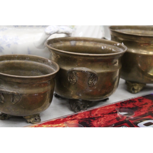 216 - THREE GRADUATED BRASS FOOTED AND HANDLED POTS