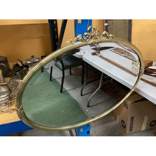 66 - A LARGE GILT FRAMED OVAL WALL MIRROR WITH A DECORATIVE RIBBON DESIGN FRAME