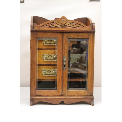 38 - A VINTAGE OAK WOOD SMOKERS CABINET WITH DOUBLE BEVELLED GLASS DOORS AND DECORATIVE BRASS HANDLES