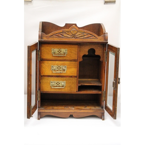 38 - A VINTAGE OAK WOOD SMOKERS CABINET WITH DOUBLE BEVELLED GLASS DOORS AND DECORATIVE BRASS HANDLES