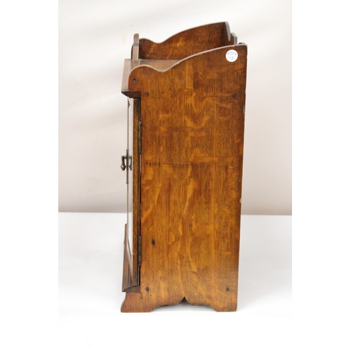 38 - A VINTAGE OAK WOOD SMOKERS CABINET WITH DOUBLE BEVELLED GLASS DOORS AND DECORATIVE BRASS HANDLES