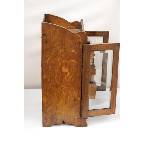 38 - A VINTAGE OAK WOOD SMOKERS CABINET WITH DOUBLE BEVELLED GLASS DOORS AND DECORATIVE BRASS HANDLES