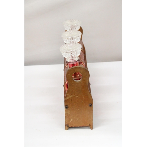 39 - A WOODEN HOLDER CONTAINING THREE AUSTRIAN STYLE 1930'S RUBY RED FLASHED ART DECO GLASS DECANTER LIQU... 