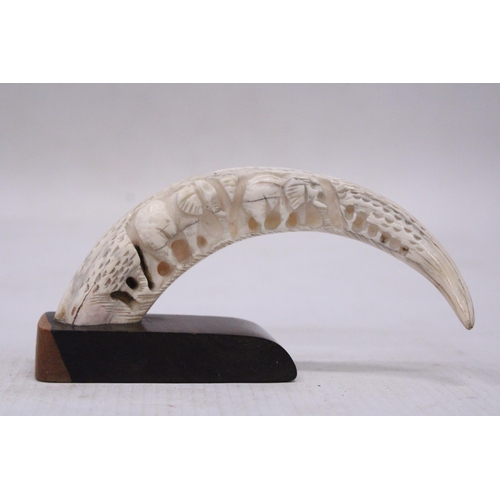 183 - A CARVED WILD BOAR TUSK ON A WOODEN PLINTH