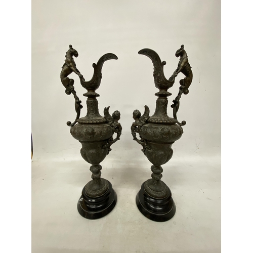 87 - A PAIR OF CAST DECORATIVE EWERS WITH CHERUBS ON A BASES HEIGHT 54CM