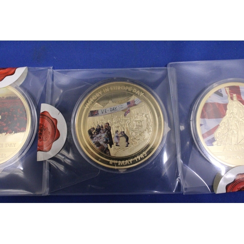 488 - THREE LARGE GOLD PLATED COMMEMORATIVE COINS TO INCLUDE A REMEMBERANCE DAY, AN ARMISTICE AND A VE DAY... 