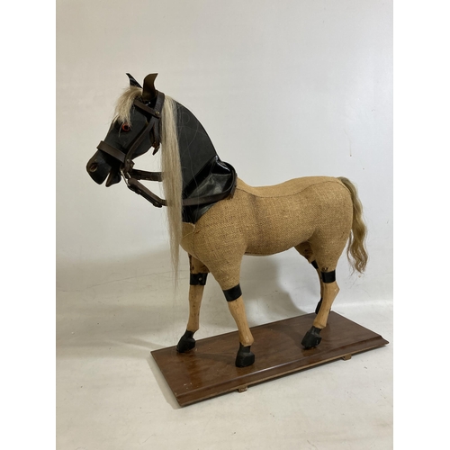 42 - A VINTAGE WOODEN AND BURLAP HORSE ON A WOODEN BASE WITH LEATHER EARS AND BRIDLE