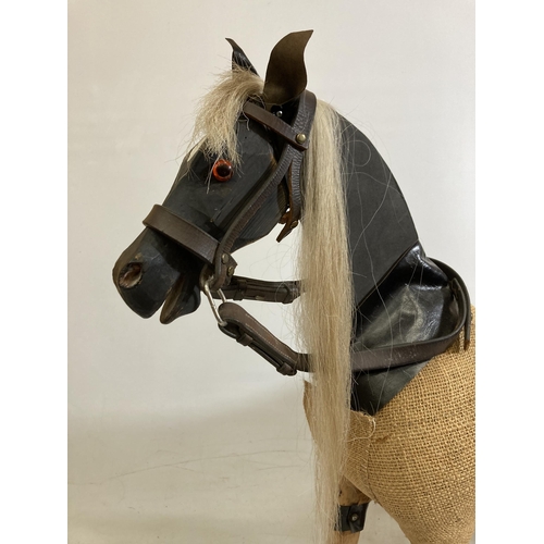 42 - A VINTAGE WOODEN AND BURLAP HORSE ON A WOODEN BASE WITH LEATHER EARS AND BRIDLE